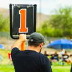 Back view of anonymous male trainer standing near scoreboard on blurred background of field during sports competition